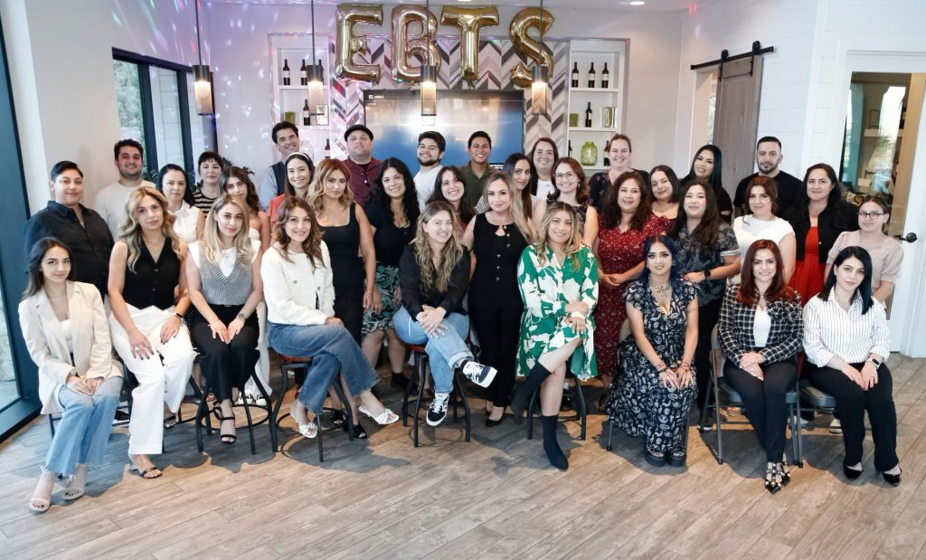 A group of people posing for a photo in a well-lit room with balloon letters spelling "EBTS" in the background.